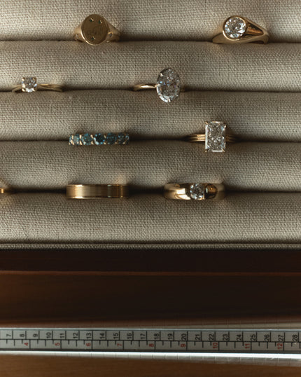 A curated flatlay of bespoke solid yellow gold rings displayed on a linen ring tray, featuring a mix of signet, solitaire, eternity and band styles with round, oval and emerald cut diamonds: handmade fine jewellery by Jade Romero, Dubai